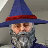 The creator, bearded and in a tall pointed hat, close to the camera in a bright attic room.