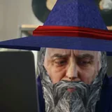 The creator at a laptop in a dim room, lit from the screen, in the same pointed hat.
